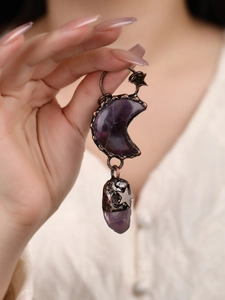 Detailed close-up of vintage bronze moon and purple crystal pendant with star motifs