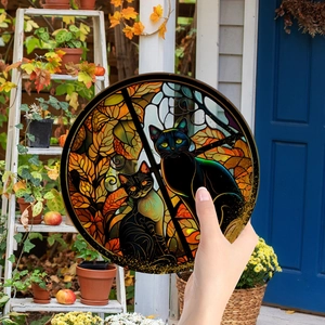 Close-up of a circular Halloween suncatcher featuring black cats and autumn leaves
