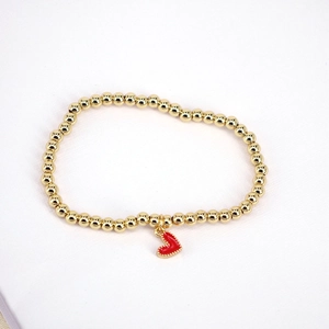 Golden beaded stretch bracelet with a red heart-shaped charm on a white background