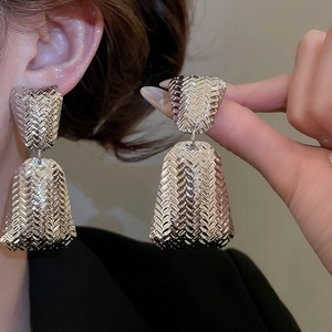 Detail view of silver metal stud earrings with woven texture worn by a model