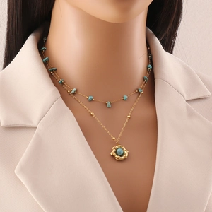 Double-layered golden necklace featuring turquoise stones and flower pendant on model