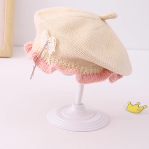Close-up of baby girl knitted beret with pink ruffle edges and lace bow detail
