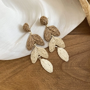 Macro detail of Bohemian raffia leaf earrings with golden metal loops on white fabric