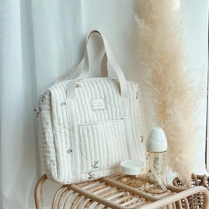 Quilted cotton mommy tote bag with olive embroidery on a rustic wicker stand