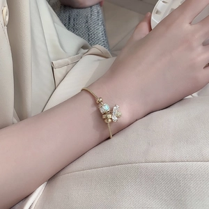 Close-up of golden snake chain bracelet featuring bee charm and rectangular crystal