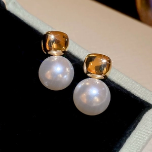 Detailed macro view of square gold studs with round white pearls on a black velvet display