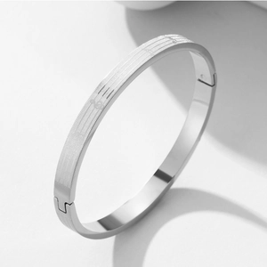 Detail of silver titanium steel bangle showing musical notes and mesh pattern etching