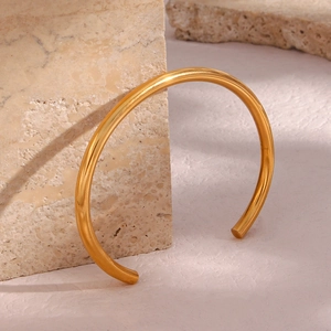 Detailed shot of a minimalist 18K gold plated open bangle on a marble stone base