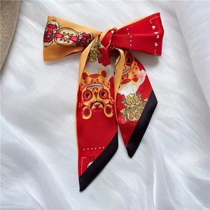 Detail of a red and gold silk skinny scarf tied in a bow with traditional lion patterns