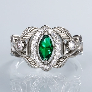 Macro detail of marquise-cut emerald ring with hollow leaf patterns and diamond accents