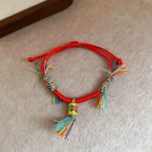 Détail du bracelet en corde rouge tissée à la main avec pendentif moulin à prières