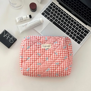 Flat lay of red checkered quilted makeup bag with blue bows and beauty essentials