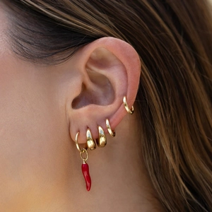 Close-up of gold hoop earrings with vibrant red chili pendants worn by a model