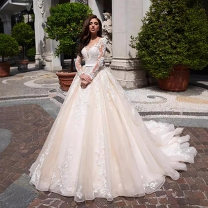 Ivory lace bridal gown with deep V-neck, long sleeves and elegant train in outdoor setting