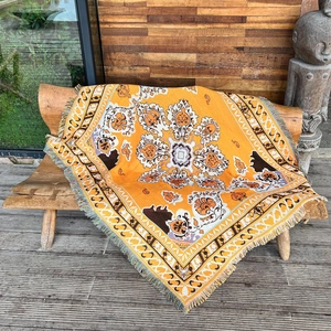 Bohemian orange mandala woven throw blanket with fringe on a wooden bench