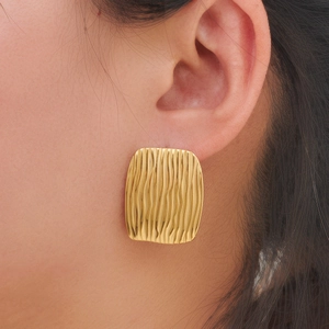 Detailed close-up of golden square stud earring with vertical wavy 3D relief texture