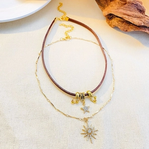 Detail of layered brown leather and gold necklace with star and sunburst pendants