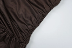 Detail of coffee brown ruched dress fabric with elegant satin sheen and elastic texture