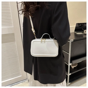 Close-up of the white suitcase-style crossbody bag with gold zippers and debossed lettering