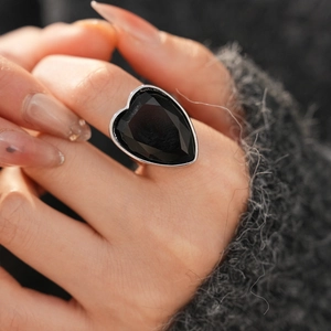 Close-up of a bold silver heart ring with black stone worn over a grey knit sweater
