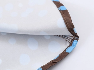 Close-up of blue polka dot satin fabric with white dots and durable brown hem stitching