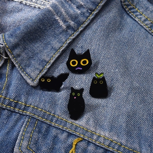 Detail of four black cat enamel pins pinned on denim fabric with sharp metallic texture