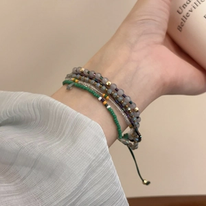 Detail of bohemian layered beaded bracelets in green and gold on woman wrist