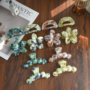 Floral resin hair claws with marble texture in green and blue on a wooden surface