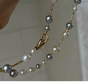 Macro detail of multi-colored pearl necklace featuring golden bars and textured hook clasp