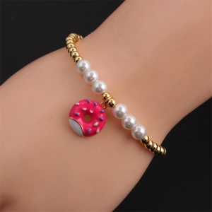 Detail of beaded bracelet featuring gold copper beads, white pearls and pink donut charm
