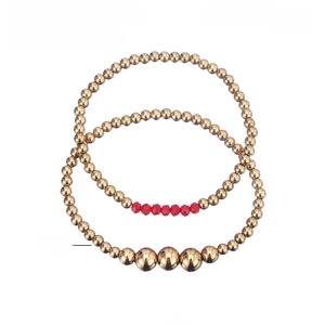 Detail view of two gold stainless steel beaded bracelets with red crystals and specs