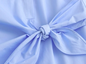Detail of light blue poplin shirt featuring a front tie-knot design and cotton texture