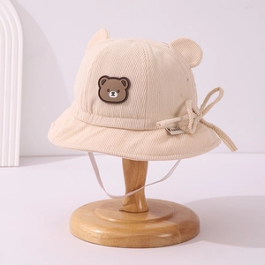 Detailed close-up of baby corduroy bucket hat with bear patch and 3D ears on a wooden stand
