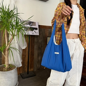 Close-up of electric blue pleated tote bag with woven label held by a model