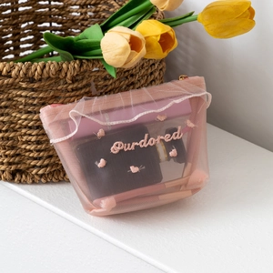 Detailed view of pink mesh makeup bag with delicate heart embroidery and zipper closure