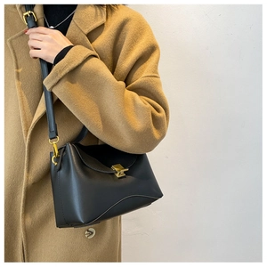 Detail of black leather shoulder bag with gold square lock on a camel coat background