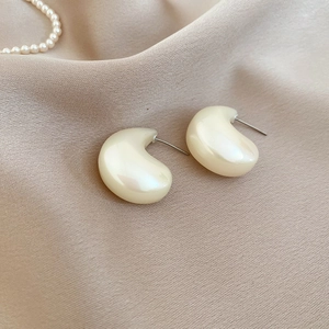 Detailed view of cream acrylic teardrop earrings with a pearl-like luster on silk