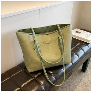 Detail of light green woven tote bag with metallic logo plate on brown leather bench