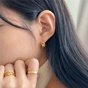 Close-up of golden knotted earrings and wave rings worn by a model for a chic look
