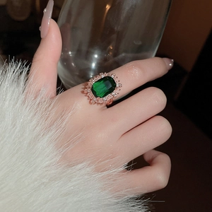 Close-up of emerald ring with rectangular cut and rose gold band on a hand