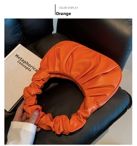 Detail of orange pleated crescent bag with cloud-like texture on a black leather background
