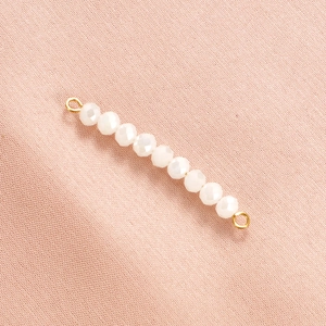 Macro shot of white faceted crystal beads with gold metal loops on pink fabric