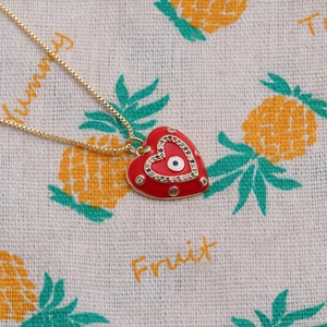 Macro detail of red heart pendant with evil eye and zircons on a gold necklace