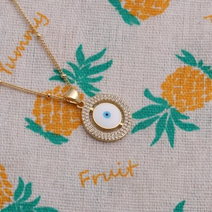 Collier avec pendentif Mauvais Œil doré et pierres en zircon sur fond décoratif