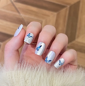 Macro detail of shimmer grey press-on nails with blue butterfly art and geometric lines