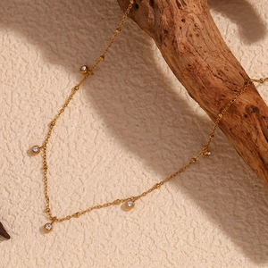 Detailed view of an 18K gold plated necklace with zircon stones on a wooden branch