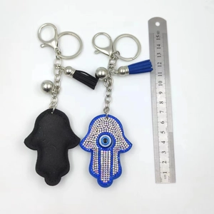 Macro detail of Hamsa Hand keychain with blue rhinestones and tassels next to a ruler