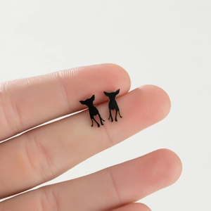 Detail view of minimalist black chihuahua silhouette stud earrings held by hand