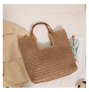 Flat lay of a woven straw tote bag with brown leather handles on white textured fabric