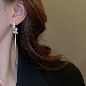Close-up of elegant knotted tassel earrings with zircon inlay worn by a female model